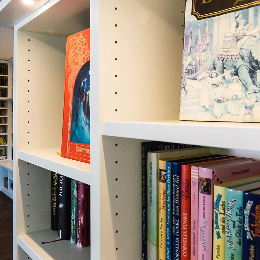 Bunte Büchersammlung in einem modernen Regal Offenes Regalsystem in einem hellen Raum, gefüllt mit einer Vielfalt an Büchern, darunter Romane und Kinderliteratur.