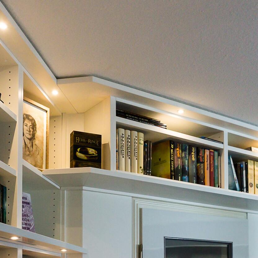 Elegantes Bücherregal über einem Kamin Weißes Bücherregal über einem modernen Kamin, gefüllt mit einer Sammlung von Büchern und dekorativen Objekten, unterstrichen durch eingebaute Beleuchtung.