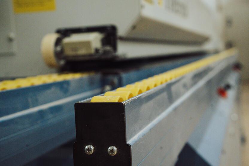 Nahaufnahme einer Kantenanleimmaschine mit einer blauen Schiene und gelben Rollen