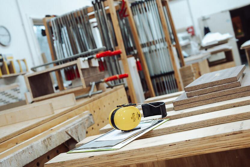 Bankraum der Tischlerei Lohse aus Kisdorf. Im Vordergrund befindet sich ein Gehörschutz auf einem Tisch. Der Hintergrund bildet einen Wagen mit Schraubzwingen