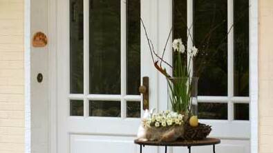 Weiße Holzhaustür mit Glasfenstern Stilvolle weiße Haustür aus Holz mit großen Glasfenstern, dekoriert mit Frühlingsblumen und Terrakottakugeln vor einem gelben Haus.