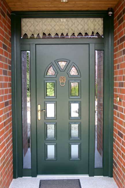 Klassische dunkelgrüne Haustür aus Holz mit dekorativen Glaseinsätzen, Löwenkopf-Türklopfer und Messinggriff, eingerahmt von roten Klinkersteinen.