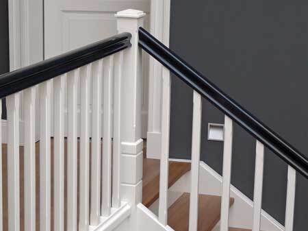 Perspektivische Aufnahme eines stilvollen Treppengeländers in Weiß mit einem kontrastierenden schwarzen Handlauf vor einer dunkelgrauen Wand.