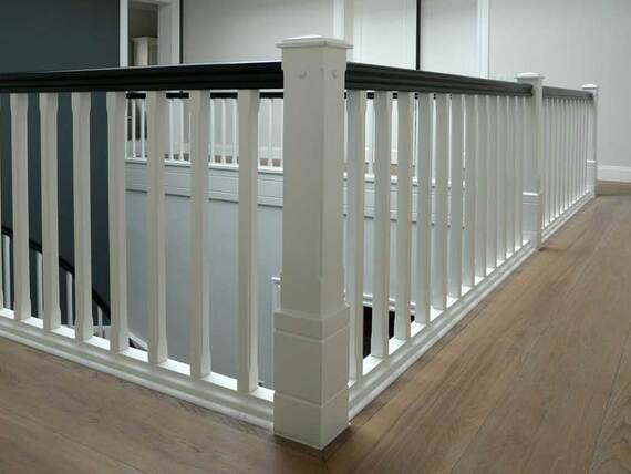 Ein modernes weißes Treppengeländer mit dunkler Handlaufkante an einem hellen Holzfußboden.