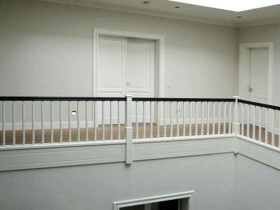 Elegantes Innenraumdesign mit einem weißen Treppengeländer, das mit schwarzen Handläufen versehen ist, umgeben von Türen und hellen Wänden.