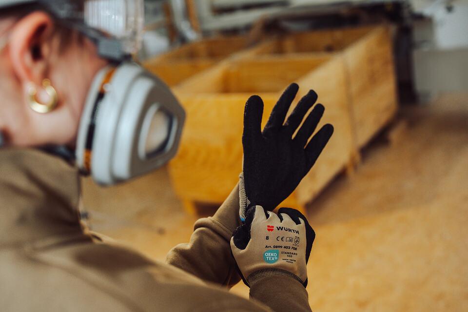 Arbeitshandschuhe Im fordernde Teil des Bildes ist eine Atemschutzmaske abgebildet. Im hinteren Teil sind Handschuhe zu sehen. Das gesamte Bild ist in beige und schwarz gehalten
