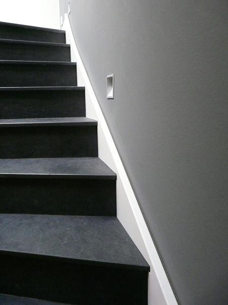 Detailaufnahme einer Treppe mit schwarzen Holzstufen neben einer grauen Wand