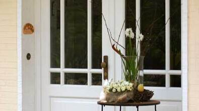 Weiße Holzhaustür mit Glasfenstern Stilvolle weiße Haustür aus Holz mit großen Glasfenstern, dekoriert mit Frühlingsblumen und Terrakottakugeln vor einem gelben Haus.