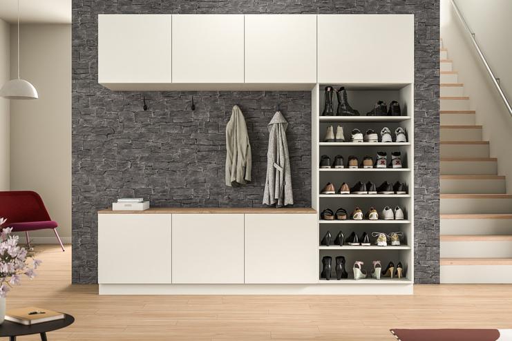 Eine stilvolle Schrankwand nach Maß in weißer Farbe mit Schubfächern und einer offenen Nische für Jacken, vor einer markanten Steinwand, im Eingangsbereich.